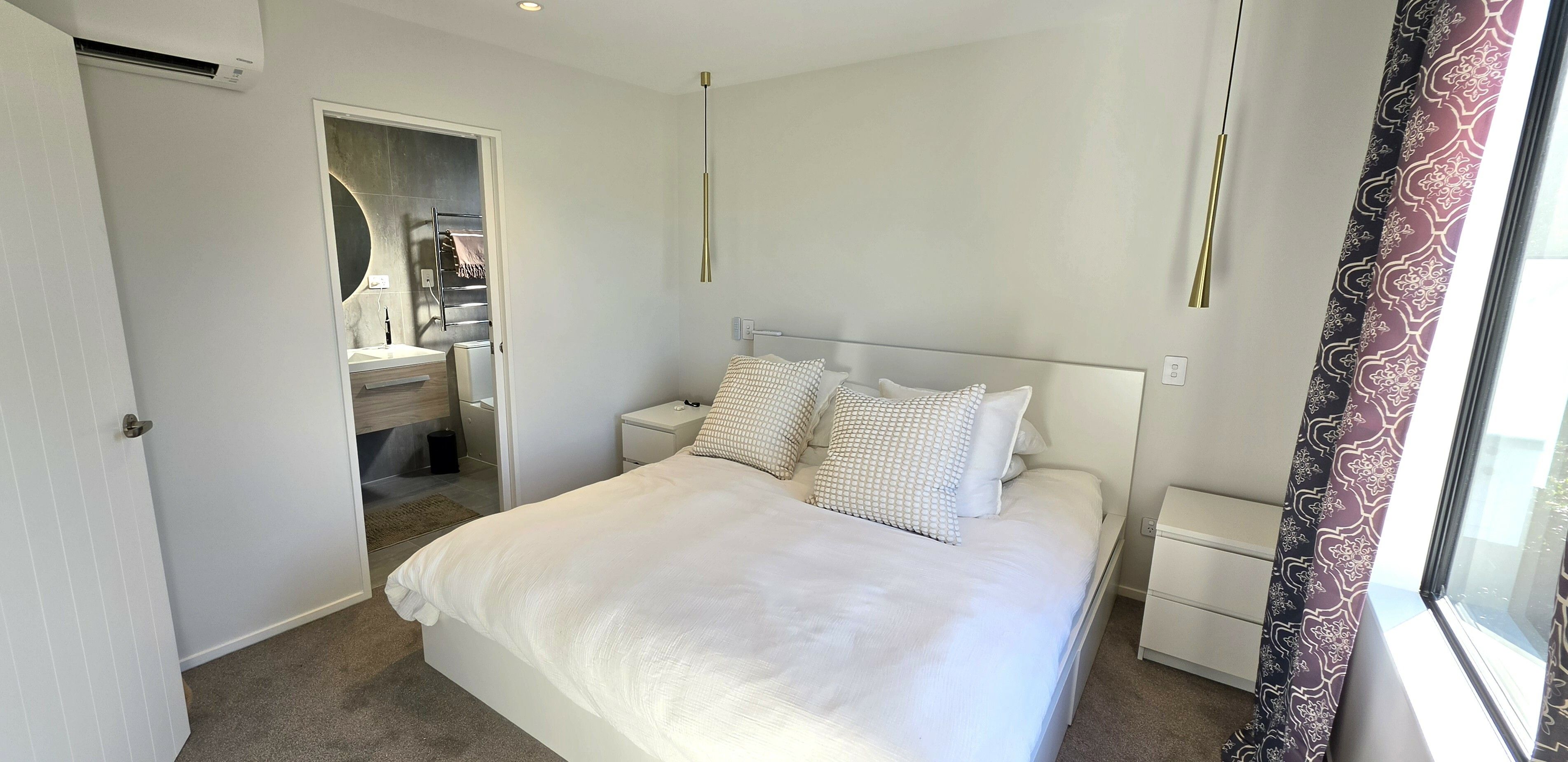 A hotel room with a bed, bedside tables, a mirror, and a window with curtains.