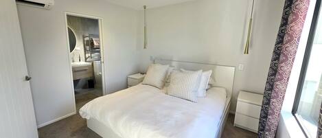 A hotel room with a bed, bedside tables, a mirror, and a window with curtains.