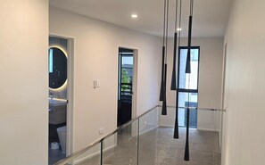 A modern interior with a glass railing, a visible bathroom with a toilet and sink, and a hallway leading to another room. - Modern 4BDR Coastal Luxury in Orakei (Auckland)