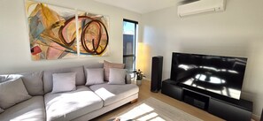 A living room with a grey sofa, a flat-screen TV, and abstract art on the wall. - Modern 4BDR Coastal Luxury in Orakei (Auckland)