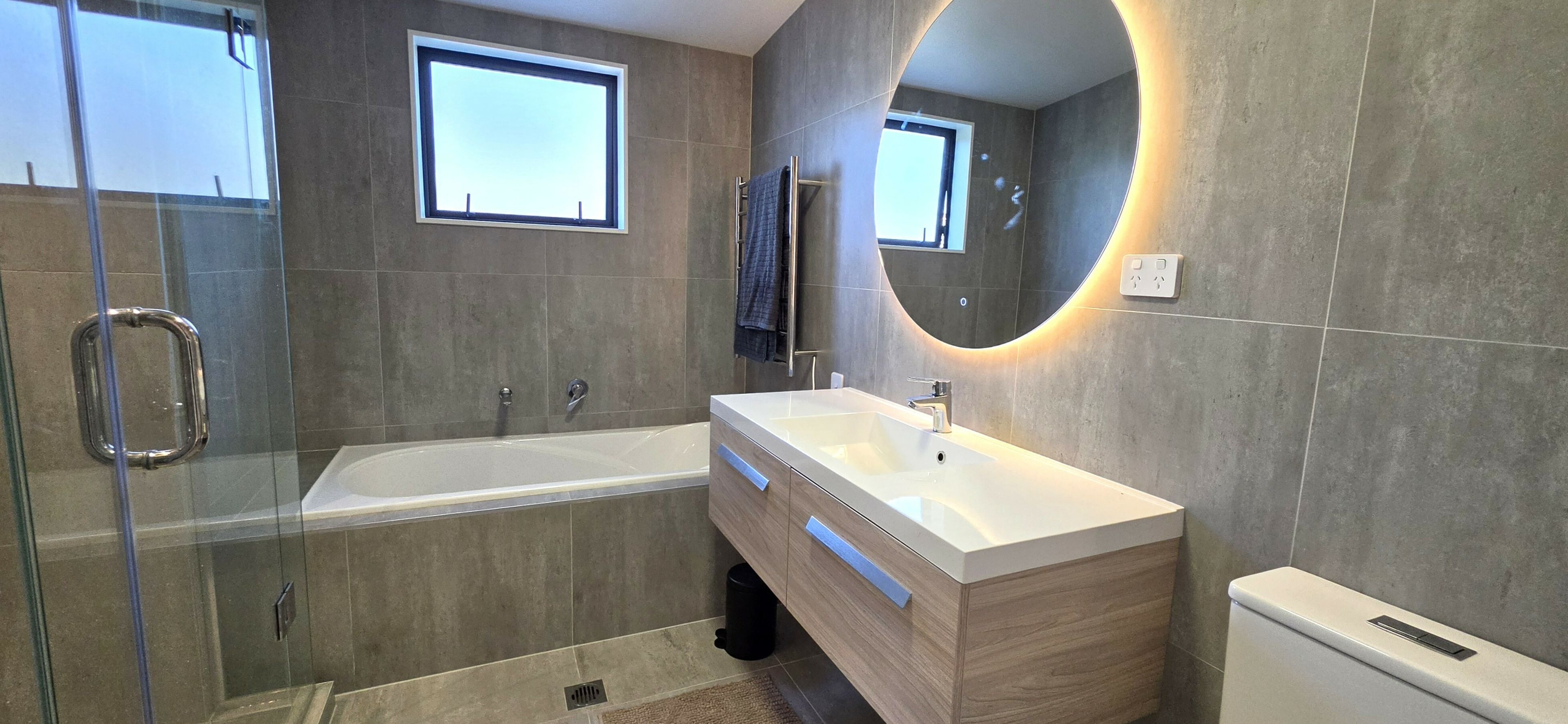 A modern bathroom with a glass shower enclosure, a freestanding bathtub, a vanity with a mirror, and a toilet.