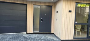 A modern building with a garage door, a door with a glass panel, and a large window with a wicker chair inside. - Modern 4BDR Coastal Luxury in Orakei (Auckland)