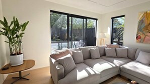 Una sala de estar moderna con un amplio sofá modular en forma de L, una pequeña mesa redonda de madera y una planta en maceta.