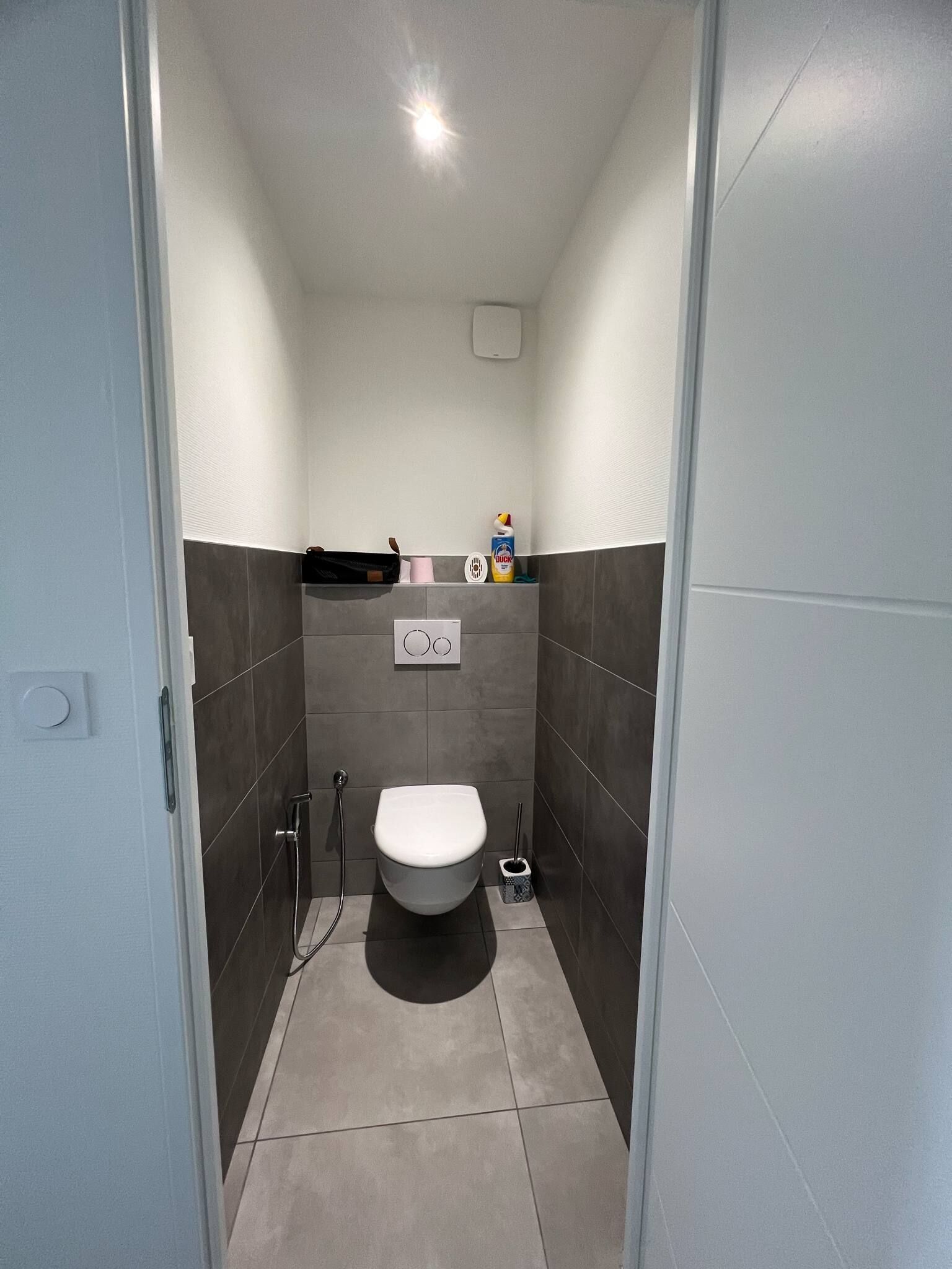Ein kleines, schmales Badezimmer mit Toilette, einem Händetrockner und einer kleinen Mülltonne.