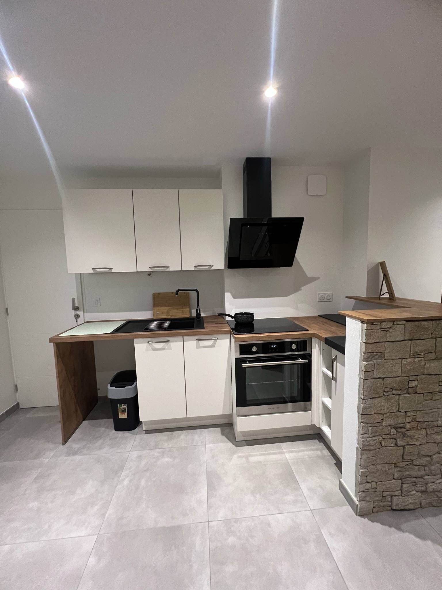 Una cocina compacta con armarios blancos, horno empotrado, estufa y una pared de acento de piedra.