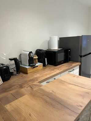 Cozinha com bancada de madeira, torradeira, chaleira, micro-ondas e frigorífico.