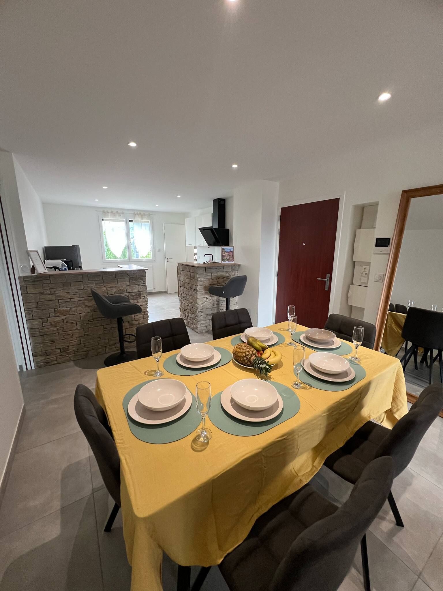 Un comedor con una mesa dispuesta para seis, una pared decorativa de piedra y una cocina al fondo.