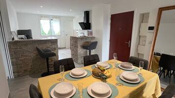 Un comedor con una mesa dispuesta para seis, una pared decorativa de piedra y una cocina al fondo.
