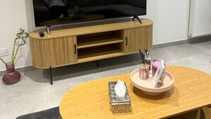 A living room with a large flat-screen TV, wooden entertainment unit, a round coffee table with decorative items, and a radiator on the wall.
