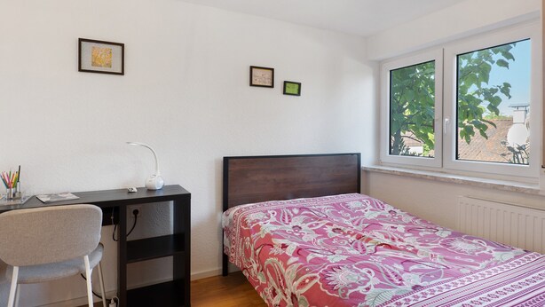 Un dormitorio con una cama, un escritorio y una silla. Hay dos cuadros en la pared.