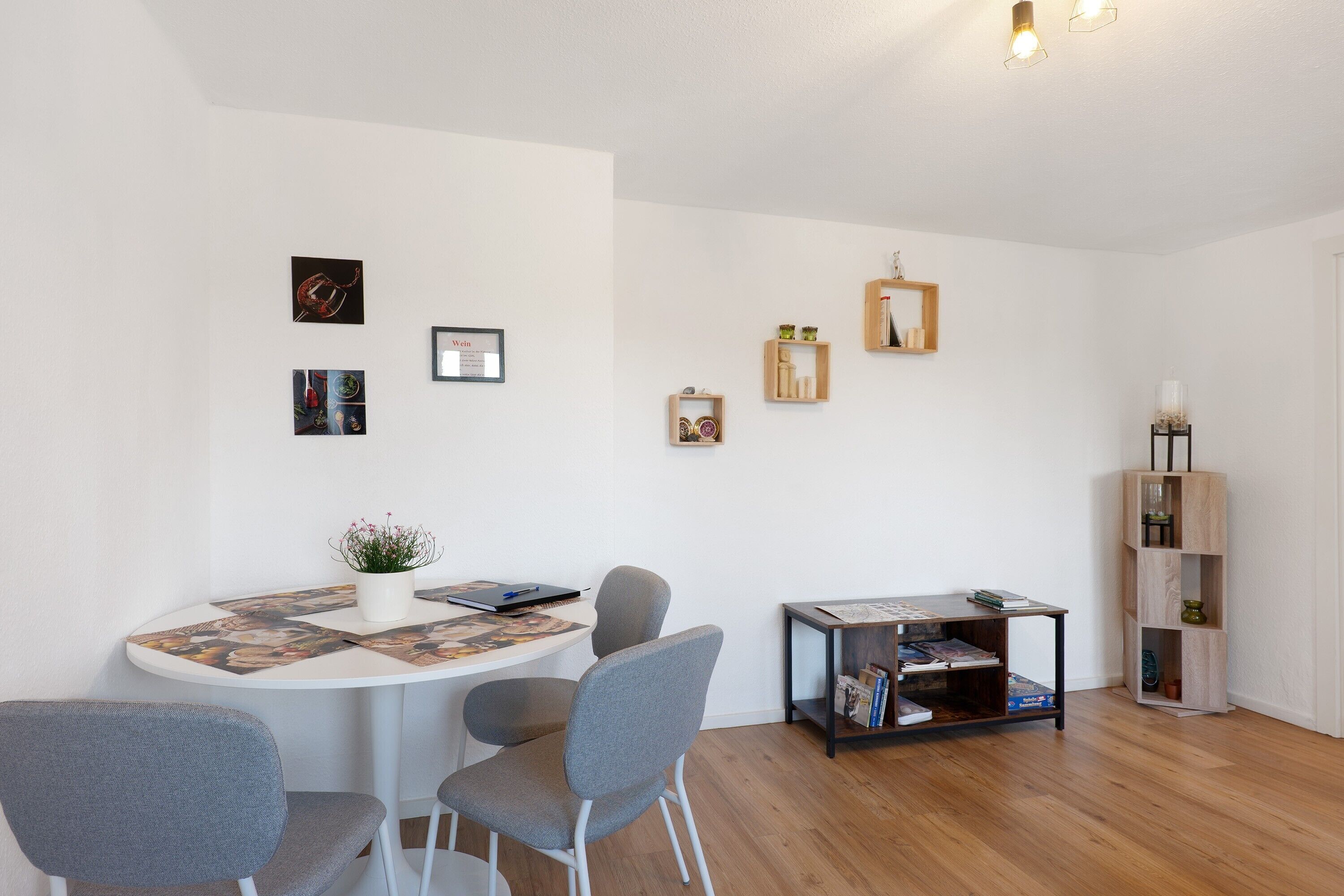 Een moderne woonkamer met een ronde eettafel, grijze fauteuils, een klein bijzettafeltje met een plant en een boekenkast met decoratieve objecten.
