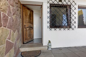 Eine Steinsäule, eine Holztür, ein Fenster mit Metallgitter, eine Fußmatte und ein kleiner Gartenzwerg.