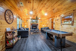 A log cabin interior with a fireplace, a pool table, and a leather sofa. - Cozy Mountain Cabin Retreat with Hot Tub, Fire Pit, and Game Room for Relaxing Getaways in Sevierville, Tennessee (Sevierville)