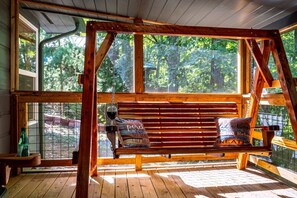 A wooden swing with cushions, a window with a view of trees, and a wooden floor. - Cozy Mountain Cabin Retreat with Hot Tub, Fire Pit, and Game Room for Relaxing Getaways in Sevierville, Tennessee (Sevierville)