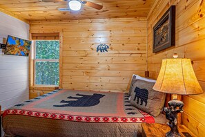Quarto de cabana de madeira com uma cama, uma luminária, uma janela e uma obra de arte na parede.