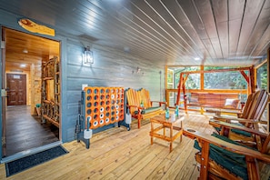 A wooden cabin interior with a wooden floor, a seating area with chairs and a table, a wooden wall with a sign, and a window with a view of greenery. - Cozy Mountain Cabin Retreat with Hot Tub, Fire Pit, and Game Room for Relaxing Getaways in Sevierville, Tennessee (Sevierville)