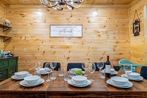 Um quarto com painéis de madeira, mesa de jantar posta para seis pessoas, um cantinho de café e uma placa na parede.