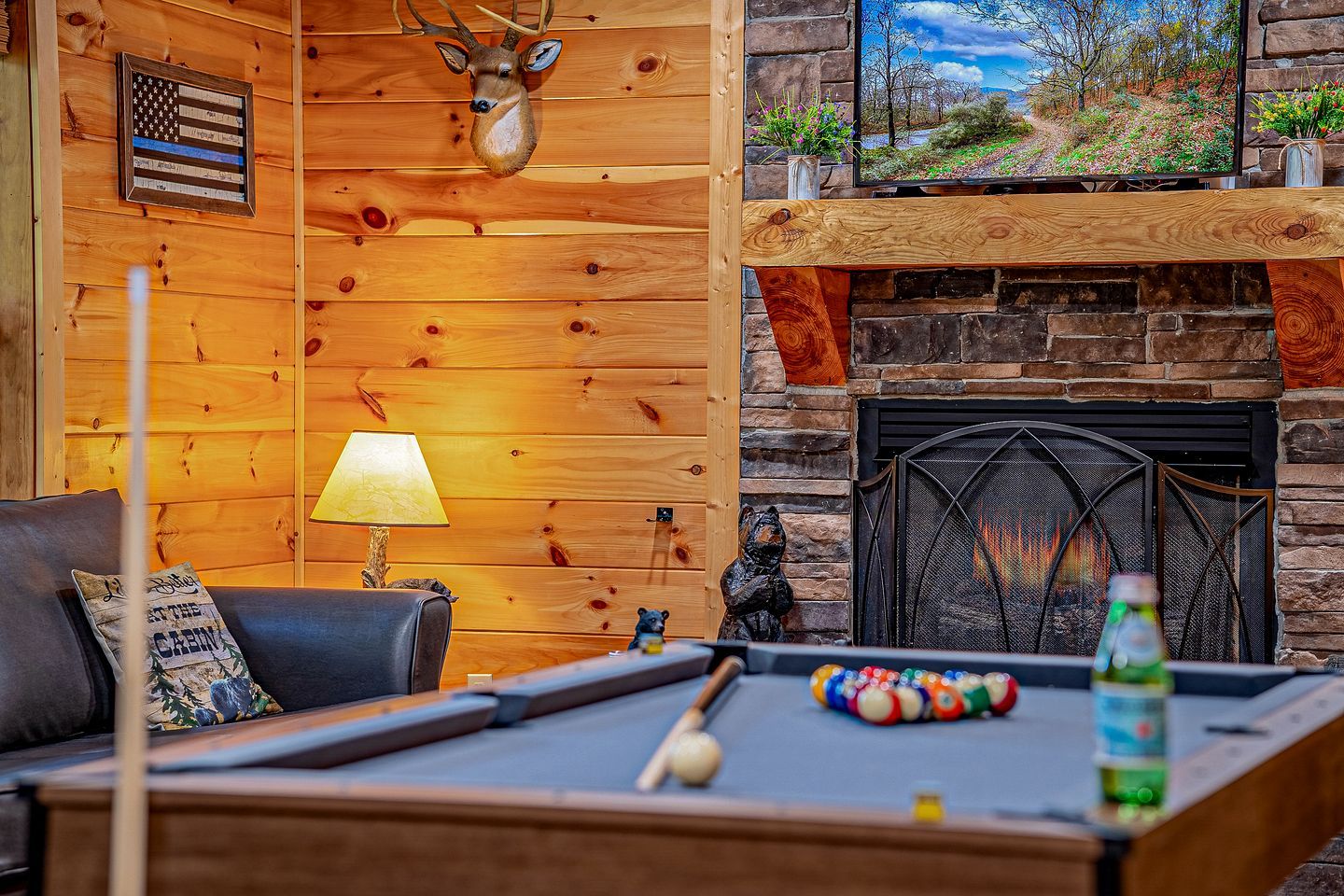 A cozy room with a pool table, a fireplace, and a television displaying a scenic view.