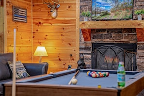 Um quarto acolhedor com mesa de bilhar, lareira e televisão exibindo uma vista panorâmica.