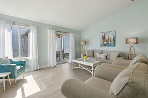 Un salon avec un canapé, une table basse, un fauteuil bleu et un tableau accroché au mur.