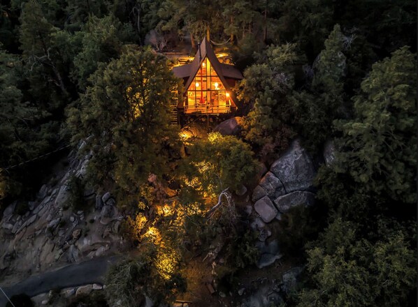 A cabin nestled in a forested area with a steep, rocky slope.