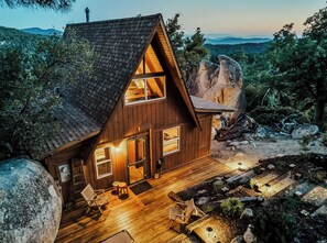 A cabin with a sloped roof, large windows, and a deck with outdoor seating.