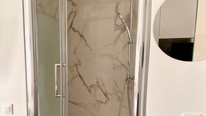 Een douche met glazen wand, een handdouche en een wandmengkraan.