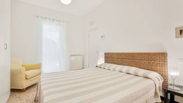 Een slaapkamer met een bed, een stoel, een radiator en een deur.