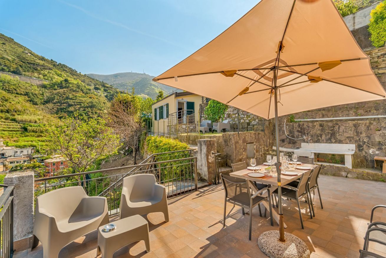 Une terrasse aménagée avec du mobilier d’extérieur, une table dressée pour le repas et un grand parasol pour faire de l’ombre.