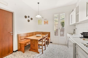 Una cucina con una panca in legno, mobili bianchi, un lavello e una porta che dà su un balcone.