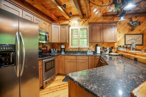 Una cocina con armarios de madera, un refrigerador de acero inoxidable, un microondas, una estufa y una ventana con persianas.