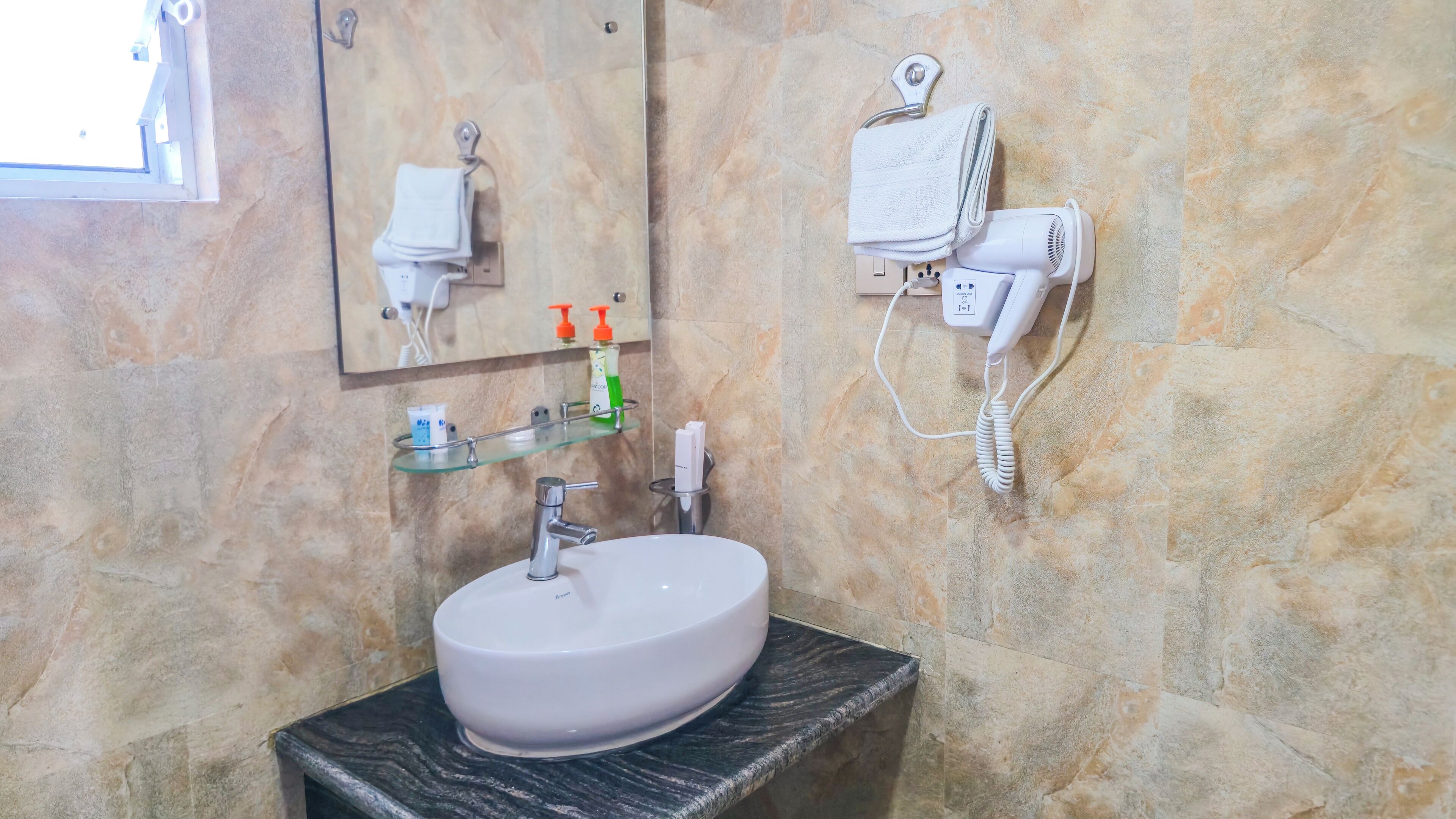 Un baño con pared de mármol, un lavabo redondo, un espejo, un perchero para toallas y un secador de pelo.