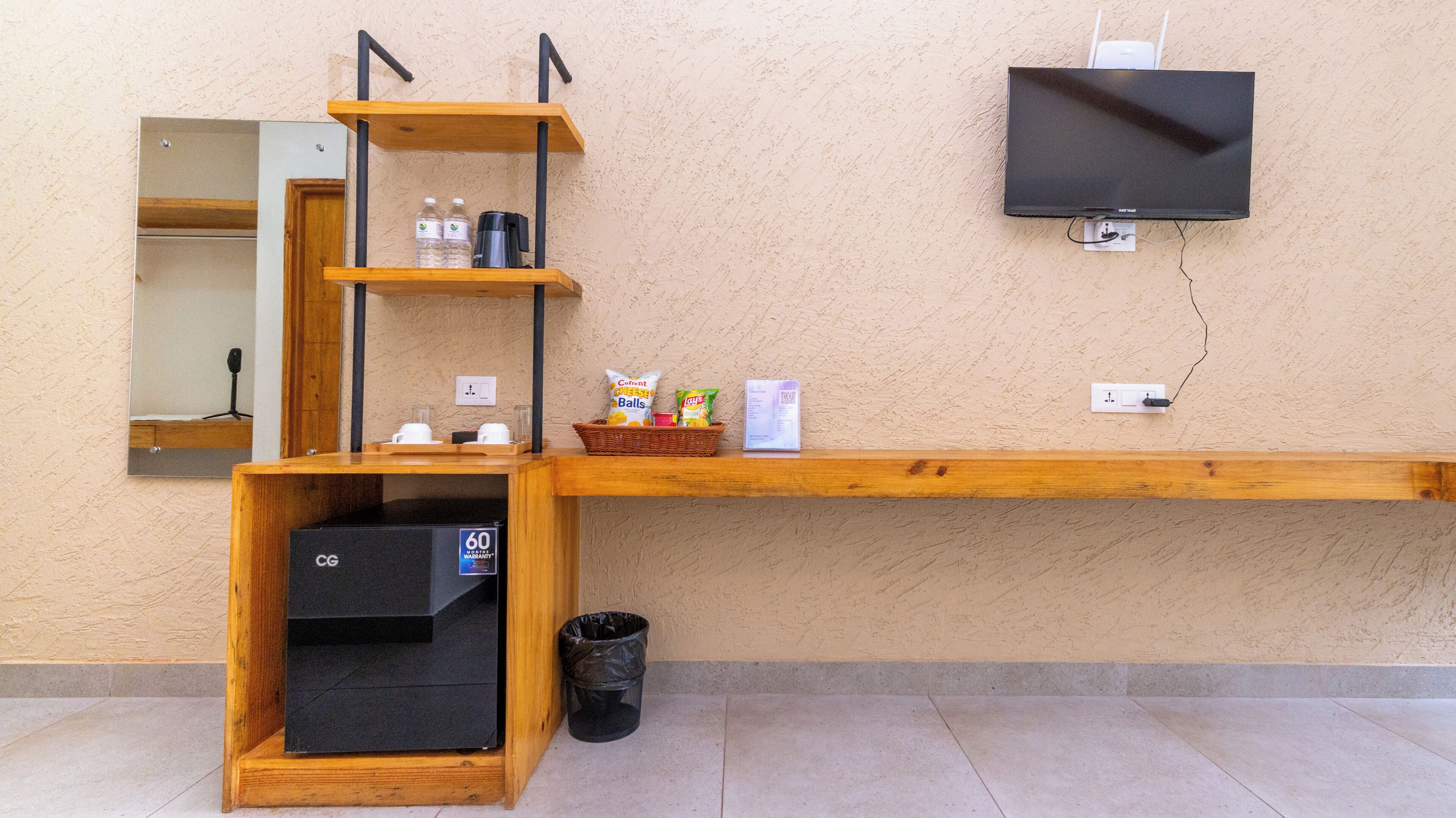 Una estantería de madera con un espejo, una caja de almacenamiento negra, un cubo de basura y un televisor de pantalla plana montado en la pared.