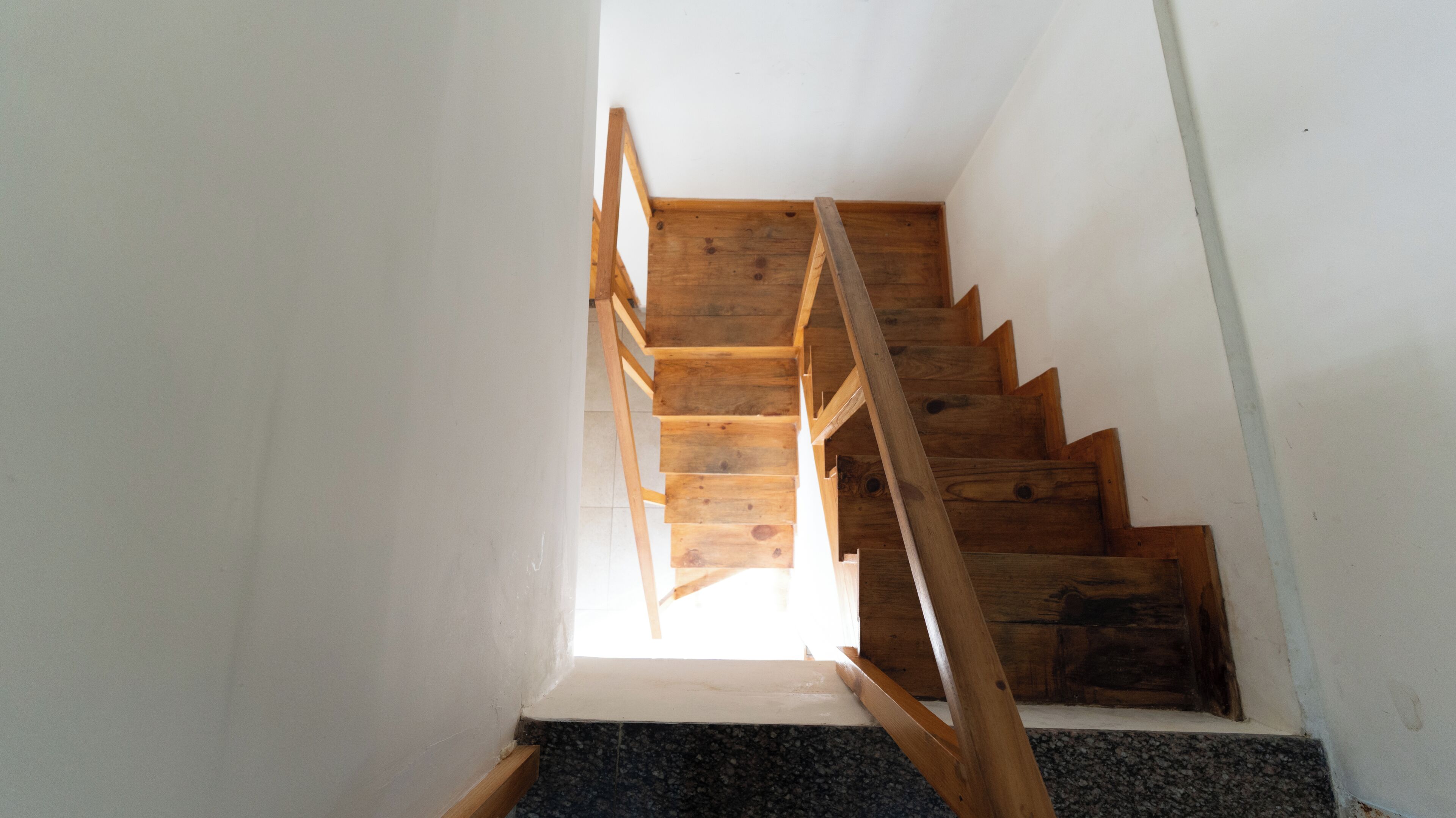 Gradians de fusta amb barana, que condueixen cap a dalt, en una habitació de parets blanques.