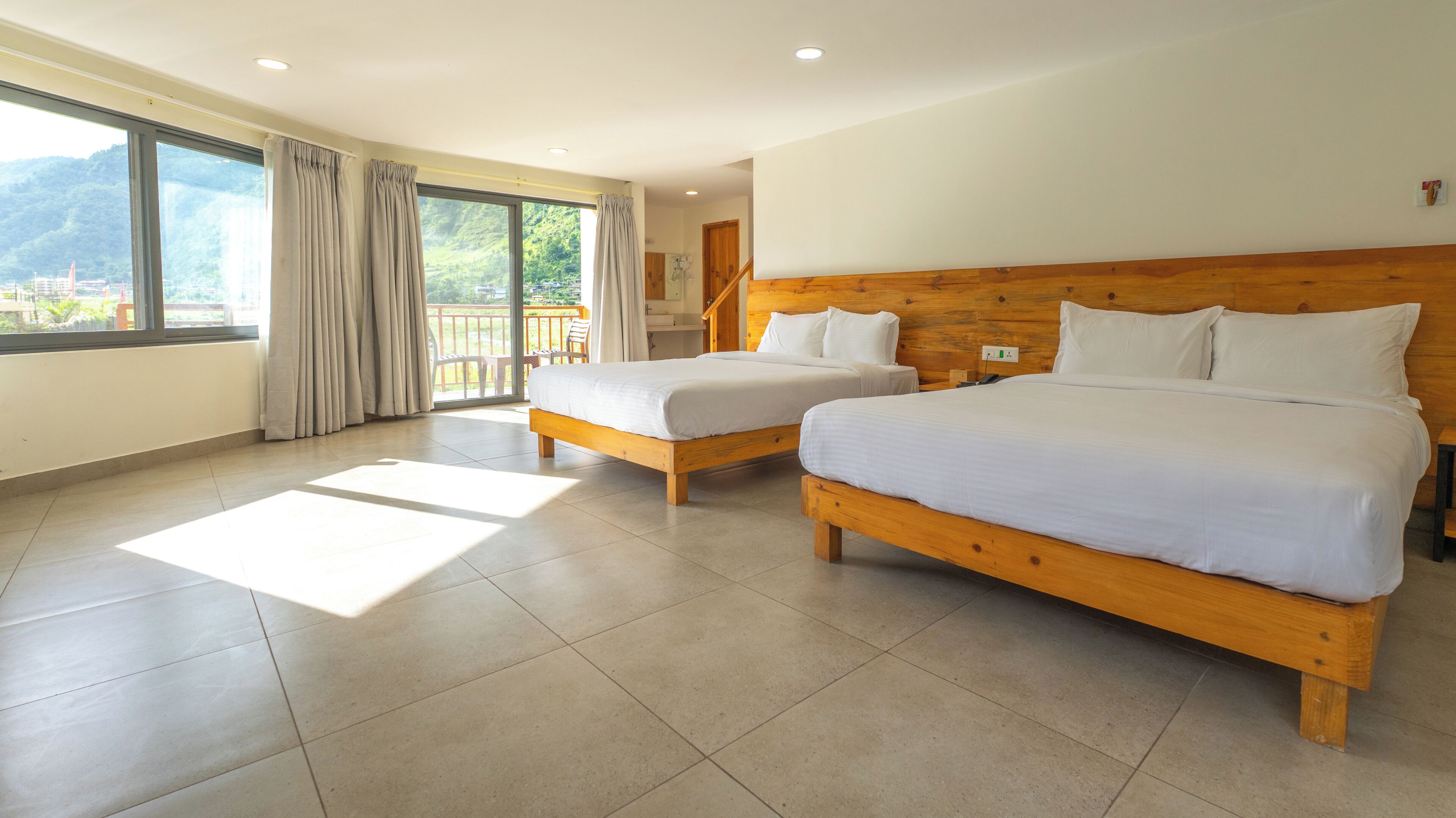 Habitació d'hotel amb dos llits, un balcó i vistes a la vegetació.