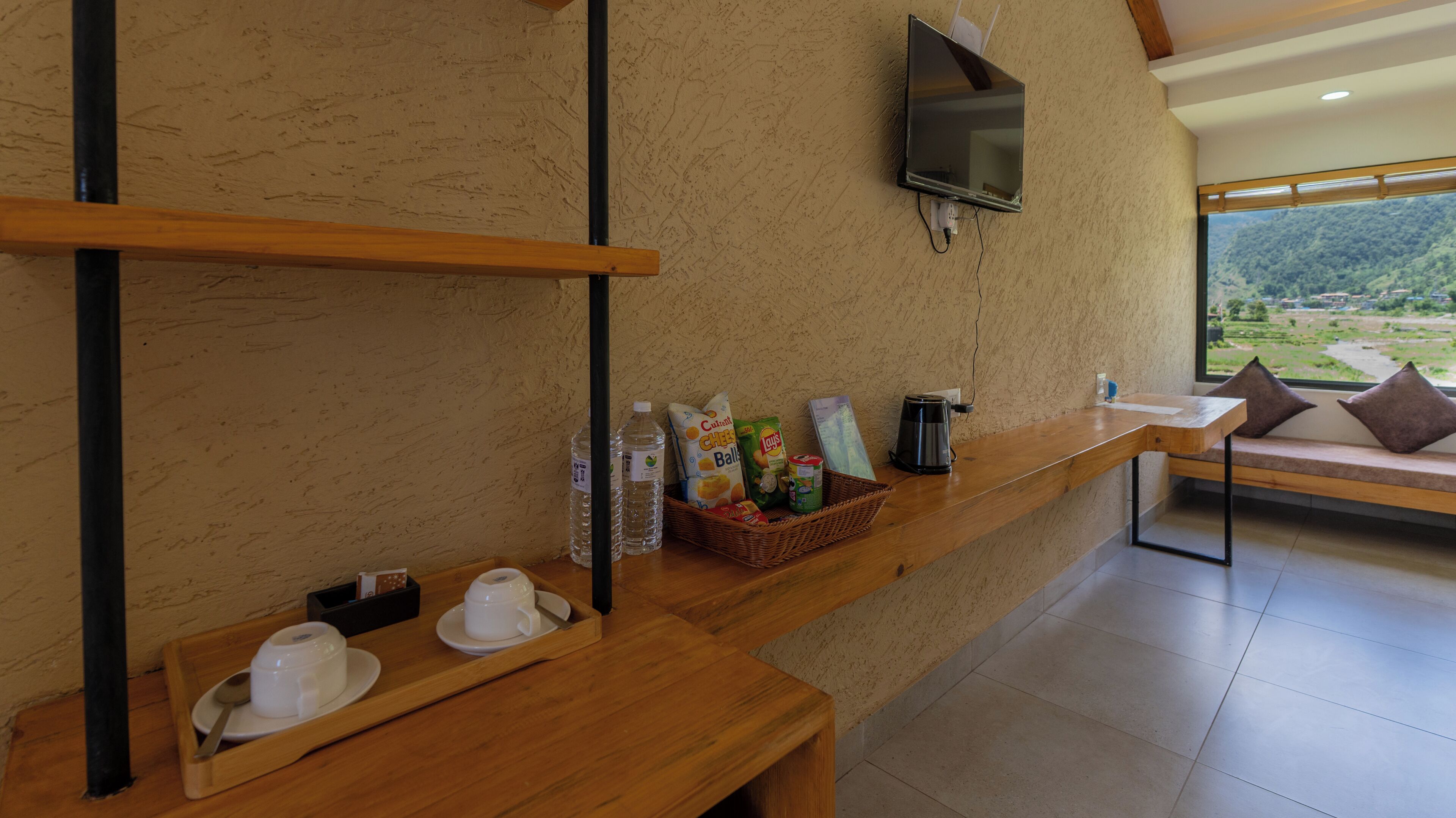 Una mesa de madera con un cesto de aperitivos, una cafetera y un televisor montado en la pared.
