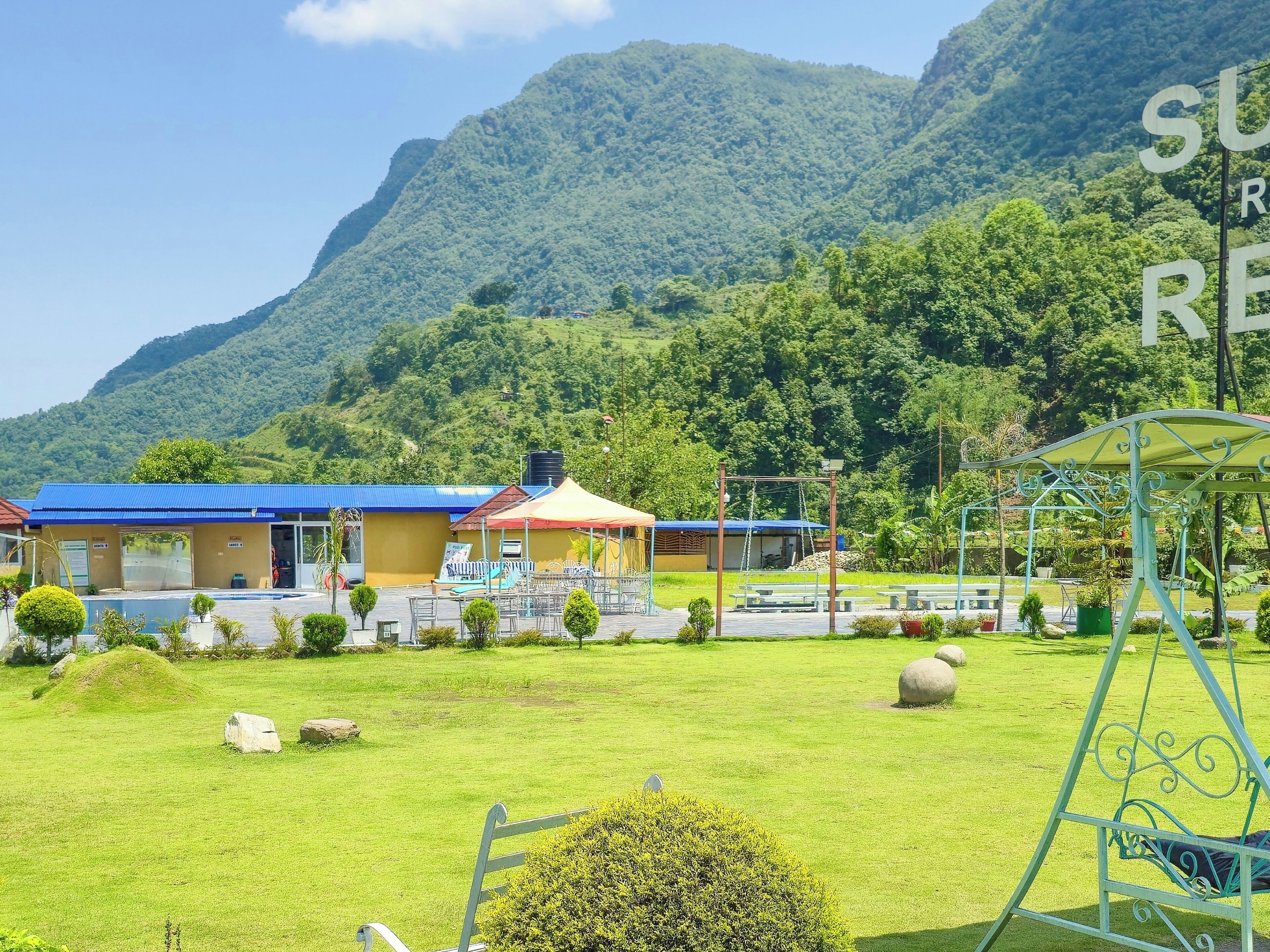 Un hotel con techo azul, un edificio rojo y amarillo, y un césped con un parque infantil.