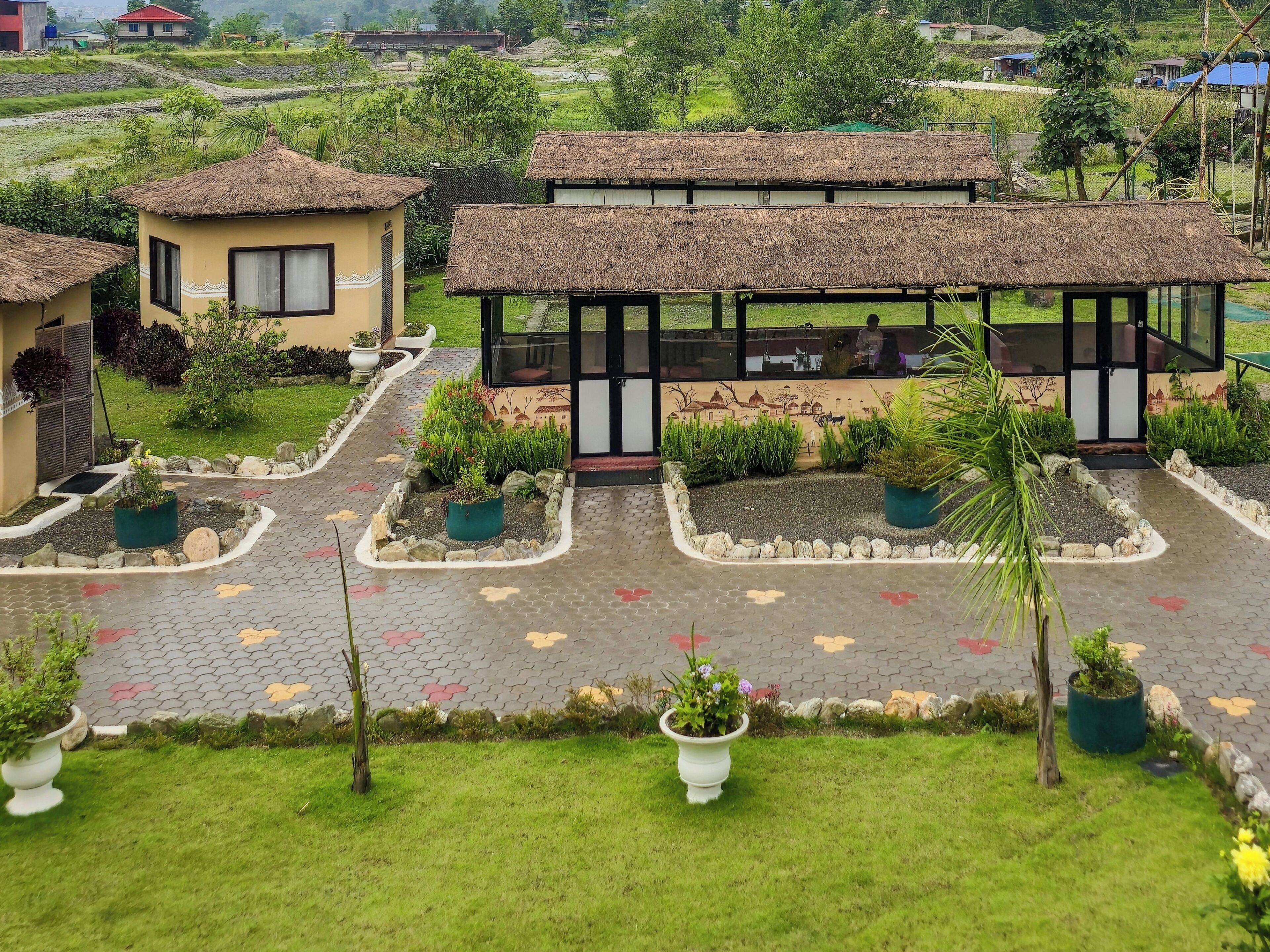 Un hotel con estructuras de techo de paja, un patio empedrado y plantas en macetas.