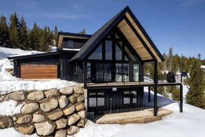 A modern two-story house with a stone wall foundation, large windows, and a wooden deck.