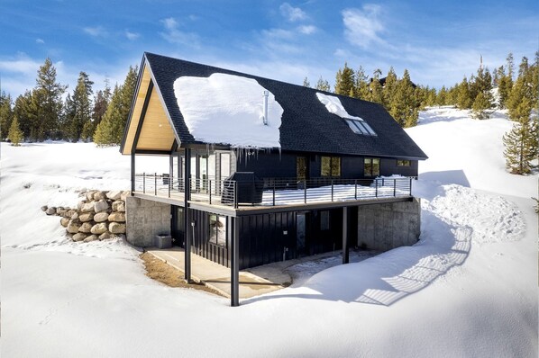 Una casa moderna de dos pisos con un balcón, rodeada de nieve y árboles.