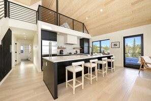 A modern kitchen with a central island, bar stools, and a view of the outdoors.