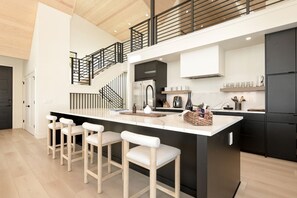 Une cuisine moderne dotée d’un îlot central, de meubles de rangement noirs et d’un escalier avec une rampe.