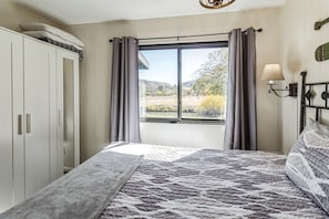 A bedroom with a bed, a window with curtains, a wardrobe, and a wall-mounted lamp. - Mountain Cabin Retreat in Greer Near Sunrise Park Resort, Arizona White Mountains (Greer)