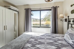 Ein Schlafzimmer mit Bett, einem Fenster mit Vorhängen, einem Kleiderschrank und einer Wandlampe.