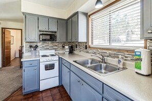 A kitchen with grey cabinets, a white stove, a microwave, a coffee maker, and a sink. - Mountain Cabin Retreat in Greer Near Sunrise Park Resort, Arizona White Mountains (Greer)