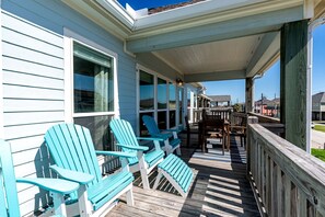 A covered porch with Adirondack chairs, a wooden deck, and a view of the street.