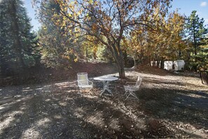 Un área de estar al aire libre con una mesa y dos sillas, rodeada de árboles con hojas otoñales.