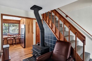 Una cocina con estufa negra, armarios de madera y una zona de comedor con sillas.