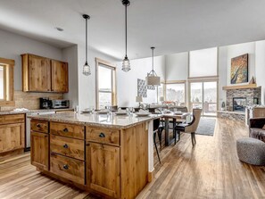 A spacious kitchen with wooden cabinets, a large island, pendant lights, and a dining area with a fireplace.