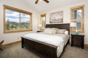 Une chambre dotée d’un grand lit, de deux tables de chevet, d’un ventilateur de plafond et de grandes fenêtres offrant une vue sur un paysage.